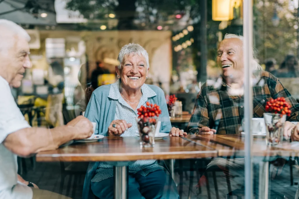 Smiling senior woman wearing a light blue blouse and blue sweater, sits at a table in a cafe, facing the window, overlooking the street in Clayton, MO
