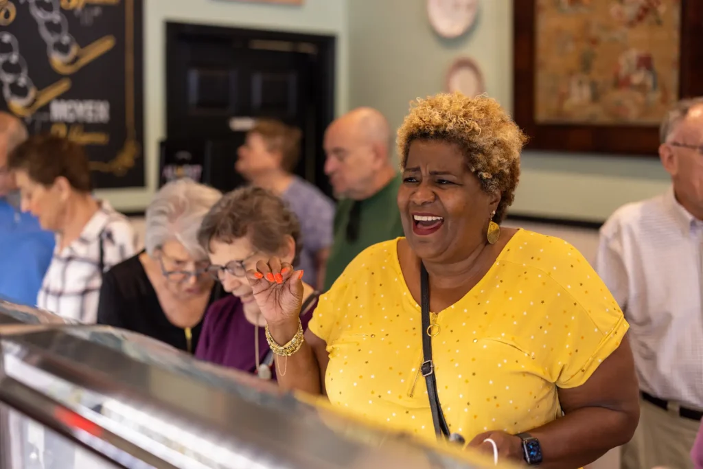smiling african american senior woman in bright yellow top orders at a counter in a Clayton ice cream shop